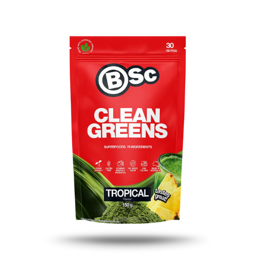 A red stand-up pouch of BSc Clean Greens Tropical powder, featuring green leaf graphics, a bowl of green powder, and pineapple slices on the front, set against a plain white background.