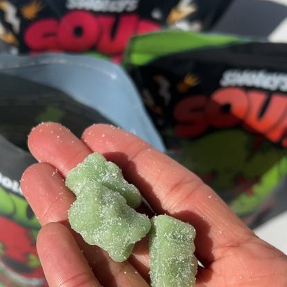 Green gummy worms held in a hand with candy packages in the background